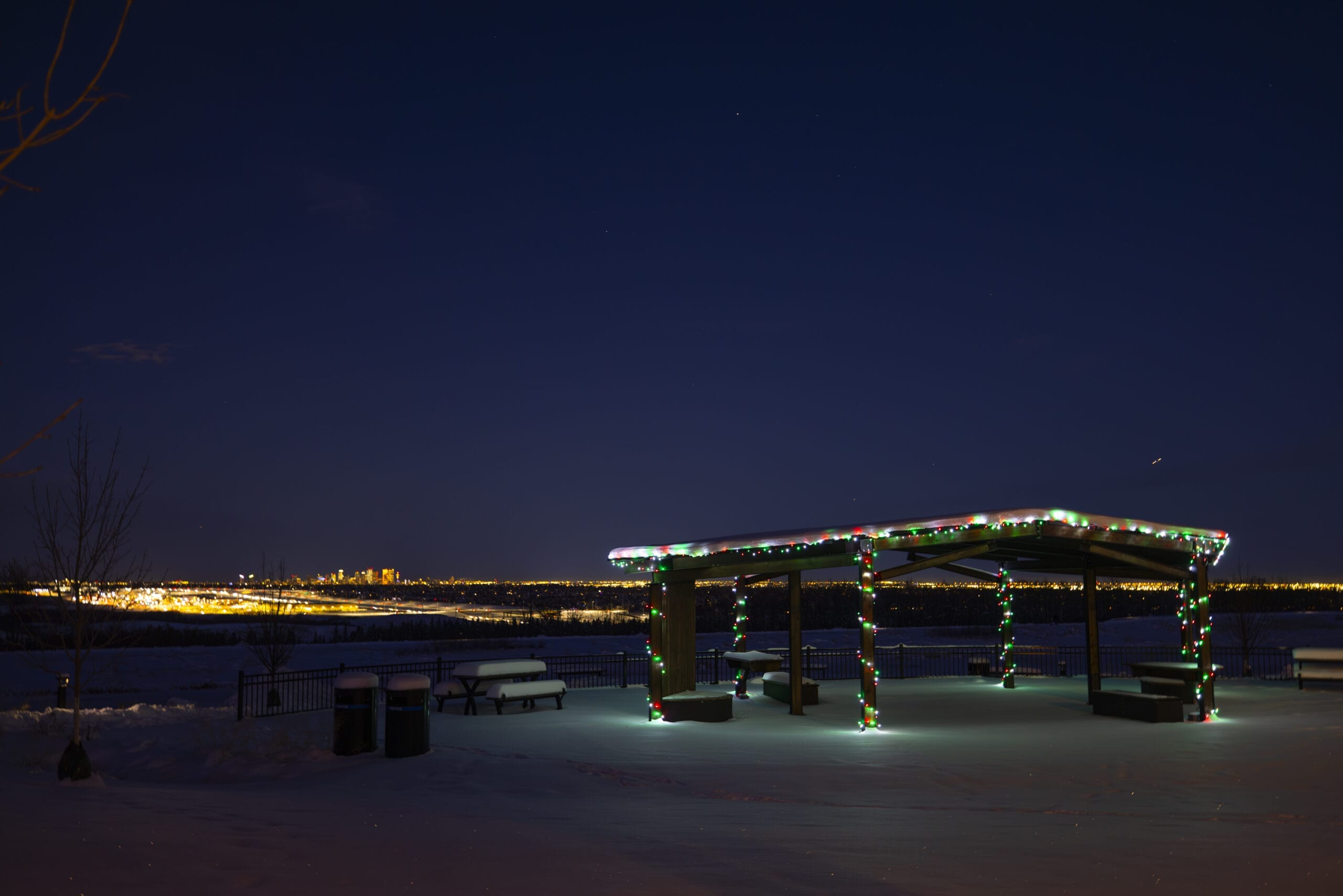 A snow-covered landscape featuring a beautifully illuminated gazebo under the night sky.