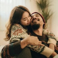 A happy couple in cozy sweaters hugging and smiling in a warmly lit living room