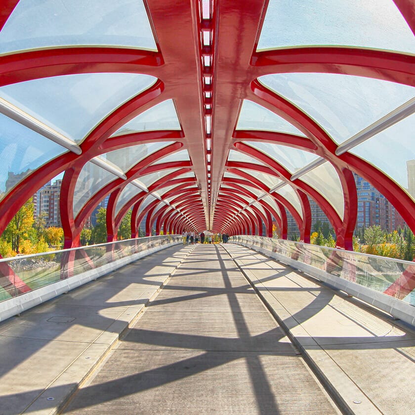 The iconic red Peace Bridge in Calgary, with its arched design and glass canopy, on a sunny day.