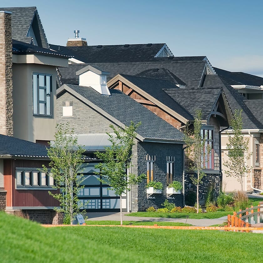 A row of modern residential homes with well-maintained yards and a clear blue sky in the background.